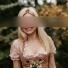 SP Escort Agency Munich, Carolin in a rose Dirndl. Her blond hair is falling over her shoulder while she stands in a garden.