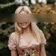 SP Escort Agency Munich, Carolin in a rose Dirndl. Her blond hair is falling over her shoulder while she stands in a garden.